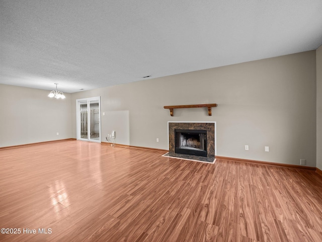 unfurnished living room with a premium fireplace, a chandelier, light hardwood / wood-style flooring, and a textured ceiling