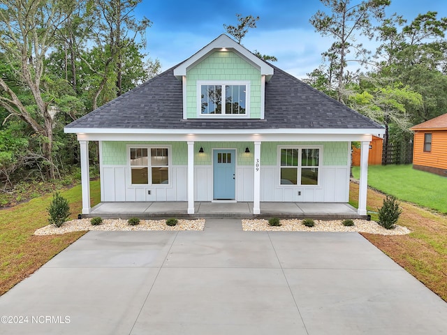 view of front of home with board and batten siding, a shingled roof, a front lawn, fence, and covered porch