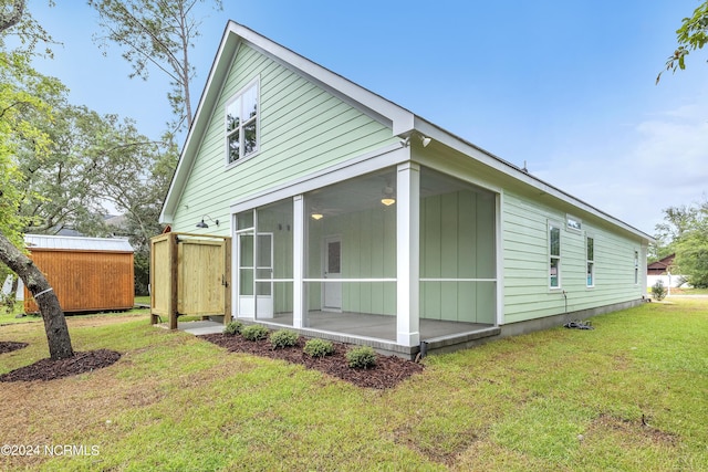 view of side of property with a storage shed, an outdoor structure, a yard, and a sunroom