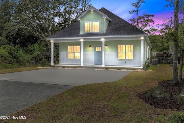 view of front facade with a lawn, covered porch, and a shingled roof