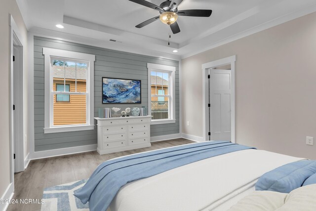 bedroom featuring a tray ceiling, wood finished floors, wood walls, baseboards, and recessed lighting
