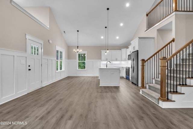 unfurnished living room featuring a notable chandelier, a sink, wood finished floors, stairway, and wainscoting