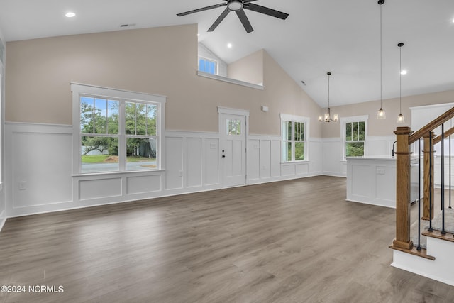 unfurnished living room with visible vents, ceiling fan with notable chandelier, wood finished floors, lofted ceiling, and stairs