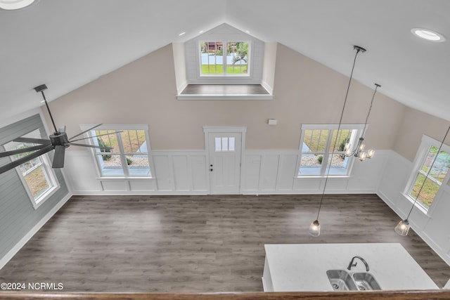 unfurnished living room featuring ceiling fan with notable chandelier, wood finished floors, a wealth of natural light, and high vaulted ceiling