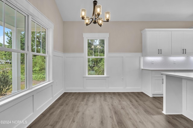 unfurnished dining area with a wealth of natural light, a decorative wall, light wood finished floors, and an inviting chandelier