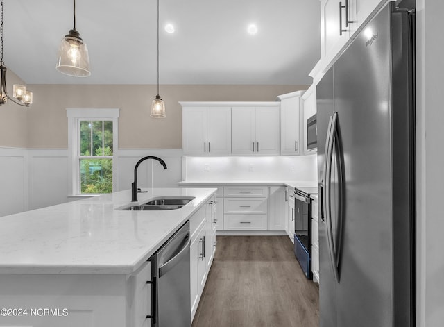 kitchen featuring a center island with sink, appliances with stainless steel finishes, wood finished floors, white cabinetry, and a sink