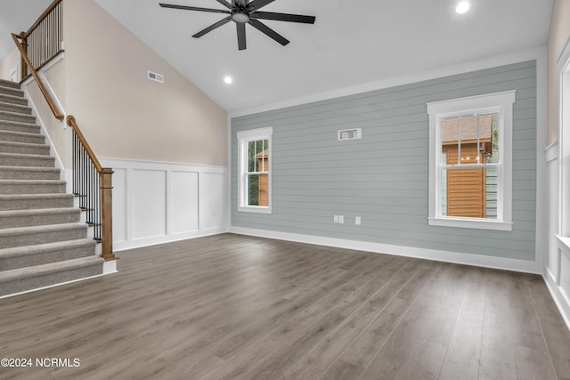 unfurnished living room with stairs, a decorative wall, a healthy amount of sunlight, and dark wood-style floors
