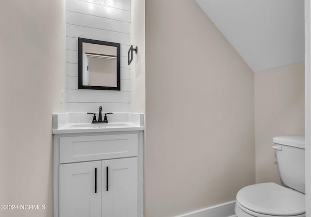 half bath featuring toilet, vaulted ceiling, and vanity