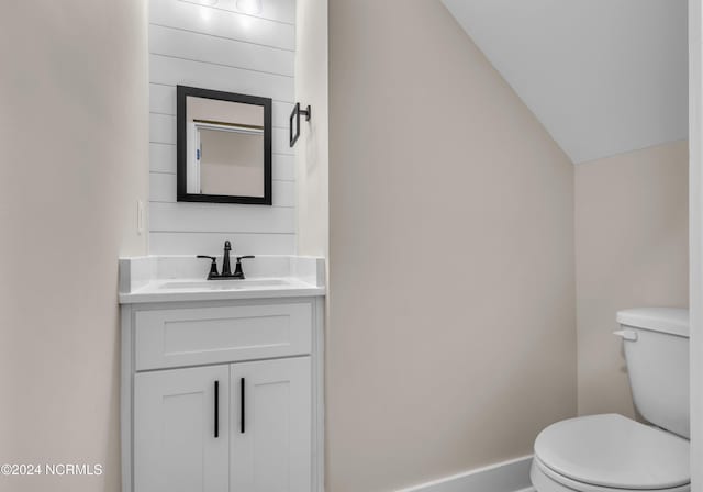 bathroom with toilet, vanity, and lofted ceiling