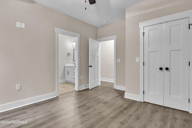 unfurnished bedroom featuring a closet, baseboards, wood finished floors, a ceiling fan, and ensuite bath