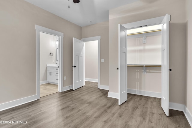 unfurnished bedroom featuring baseboards, light wood-type flooring, a closet, and ensuite bathroom