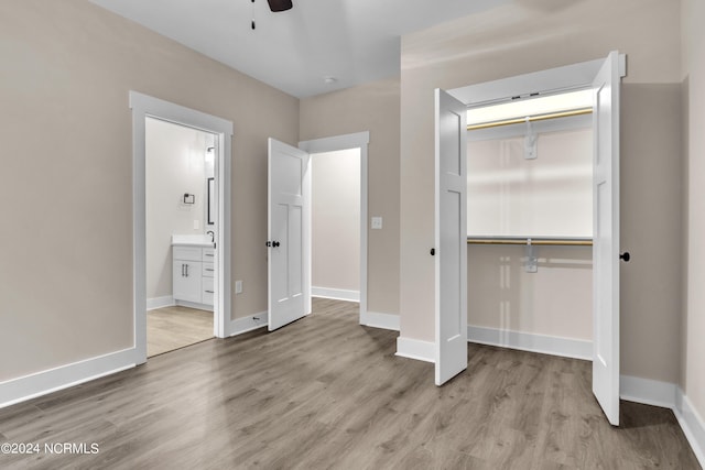 unfurnished bedroom with connected bathroom, wood finished floors, a closet, and baseboards