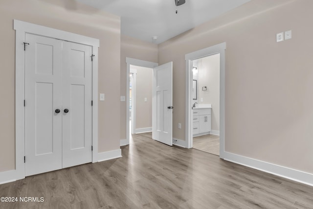 unfurnished bedroom with baseboards, ensuite bathroom, wood finished floors, and a closet