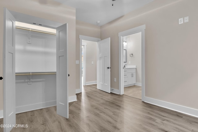 unfurnished bedroom with ensuite bath, baseboards, a closet, and wood finished floors