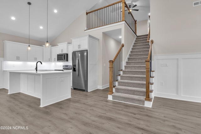 kitchen featuring light wood finished floors, appliances with stainless steel finishes, white cabinets, a decorative wall, and light countertops