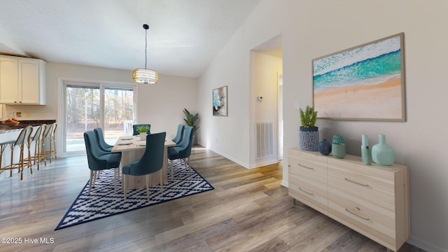 dining area featuring vaulted ceiling, a chandelier, and light wood-type flooring