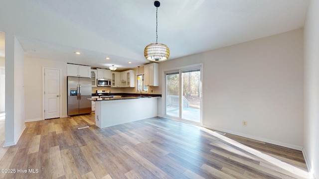 kitchen with light hardwood / wood-style flooring, appliances with stainless steel finishes, white cabinets, decorative light fixtures, and kitchen peninsula