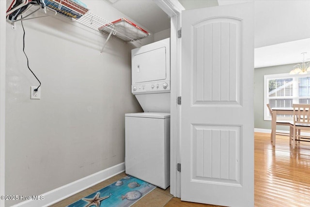 laundry area with stacked washer / dryer, a chandelier, and light wood-type flooring