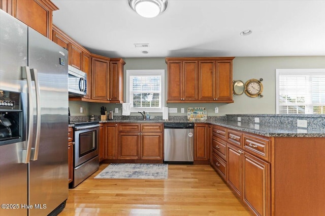 kitchen with sink, light hardwood / wood-style flooring, appliances with stainless steel finishes, dark stone countertops, and kitchen peninsula