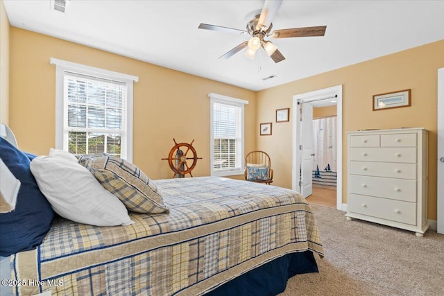 carpeted bedroom featuring multiple windows, ceiling fan, and ensuite bath