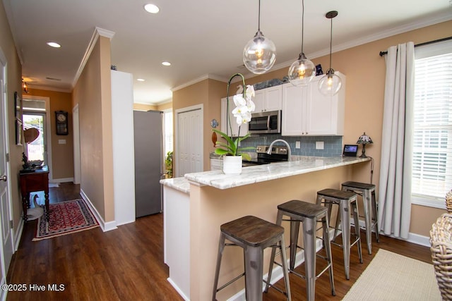 kitchen with hanging light fixtures, a kitchen breakfast bar, stainless steel appliances, white cabinets, and kitchen peninsula