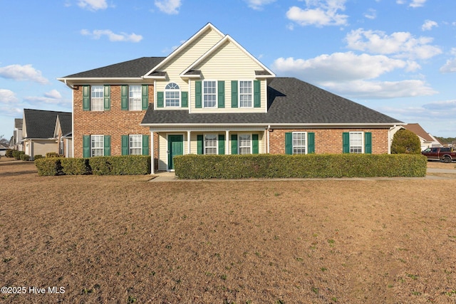 view of front of home featuring a front yard, a shingled roof, and brick siding