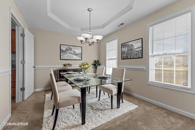 carpeted dining area featuring a chandelier, a tray ceiling, visible vents, baseboards, and ornamental molding