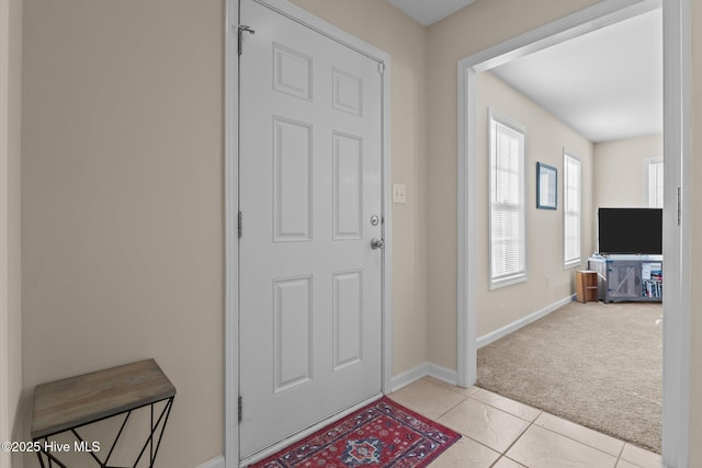 foyer with light tile patterned floors, baseboards, and light carpet