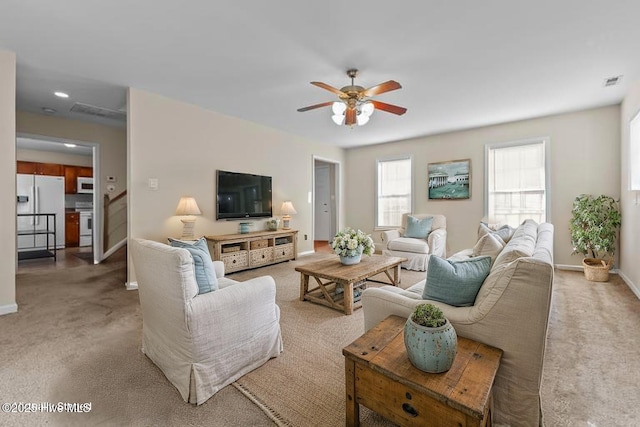 living area featuring baseboards, a ceiling fan, visible vents, and light carpet