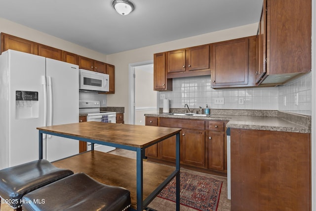 kitchen with brown cabinets, a sink, tasteful backsplash, and white appliances