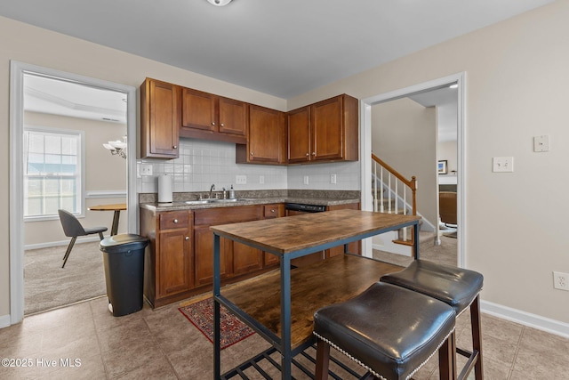 kitchen with brown cabinets, a sink, dark countertops, baseboards, and backsplash