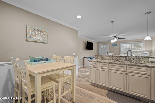 kitchen featuring sink, hanging light fixtures, ornamental molding, light stone counters, and light hardwood / wood-style flooring