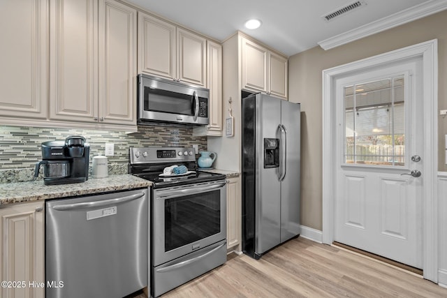 kitchen with stainless steel appliances, light stone countertops, cream cabinets, and decorative backsplash