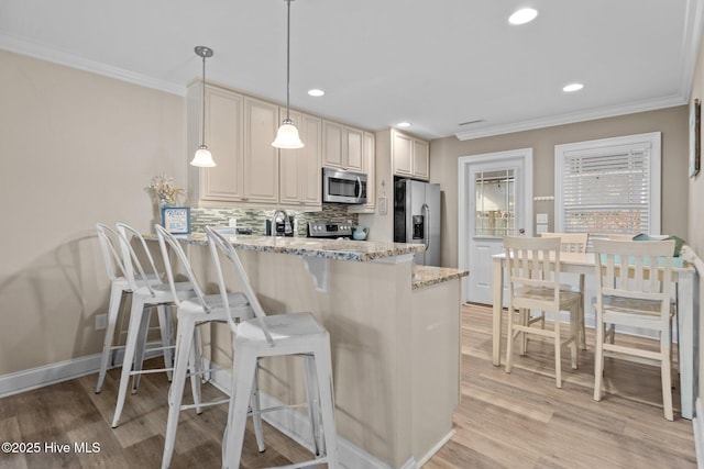 kitchen with crown molding, decorative light fixtures, stainless steel appliances, light stone countertops, and cream cabinetry