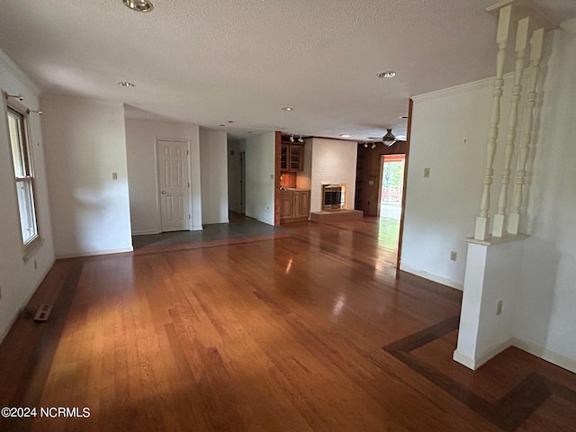 unfurnished living room with ceiling fan, a brick fireplace, a textured ceiling, and dark hardwood / wood-style flooring