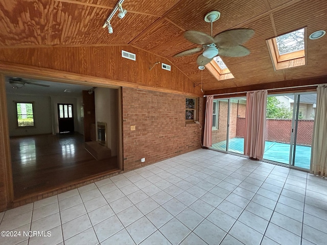 spare room with brick wall, vaulted ceiling with skylight, light tile patterned floors, and wooden ceiling