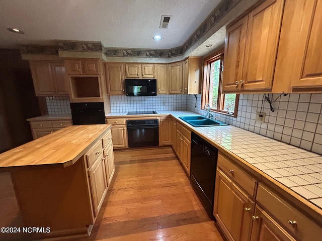 kitchen with butcher block counters, sink, a center island, light hardwood / wood-style floors, and black appliances