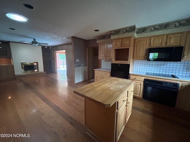 kitchen featuring dark hardwood / wood-style floors, black appliances, a large fireplace, a kitchen island, and wood counters