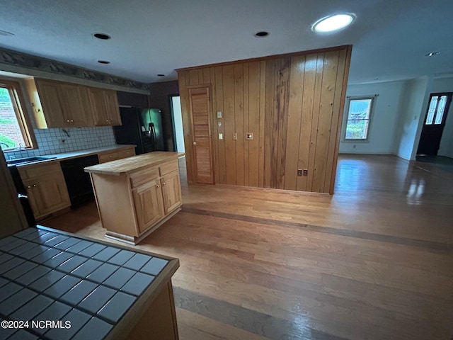 kitchen with tile countertops, tasteful backsplash, a center island, light hardwood / wood-style floors, and black appliances