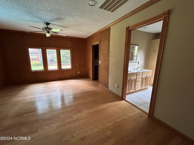 spare room with wood walls, a textured ceiling, light wood-type flooring, ornamental molding, and ceiling fan