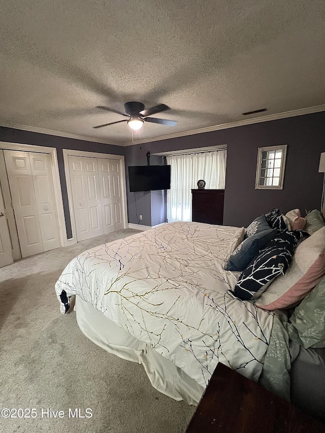 carpeted bedroom featuring crown molding, a textured ceiling, visible vents, and multiple closets