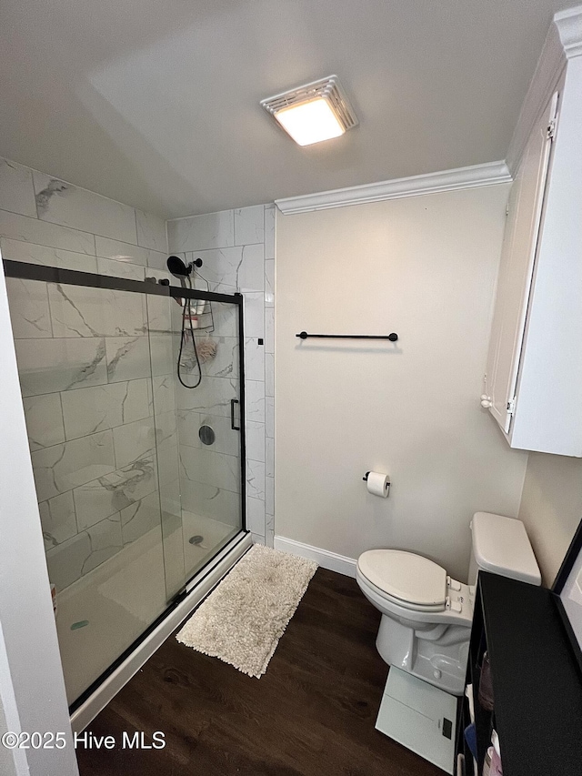 bathroom featuring toilet, wood finished floors, baseboards, ornamental molding, and a shower stall