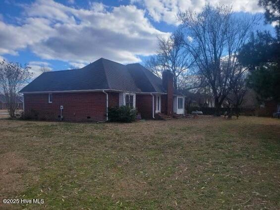 view of home's exterior with crawl space, brick siding, a yard, and a chimney