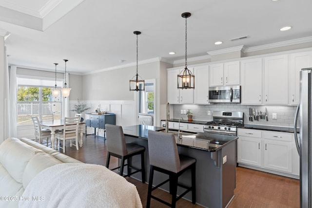 kitchen featuring white cabinetry, appliances with stainless steel finishes, an island with sink, dark countertops, and pendant lighting