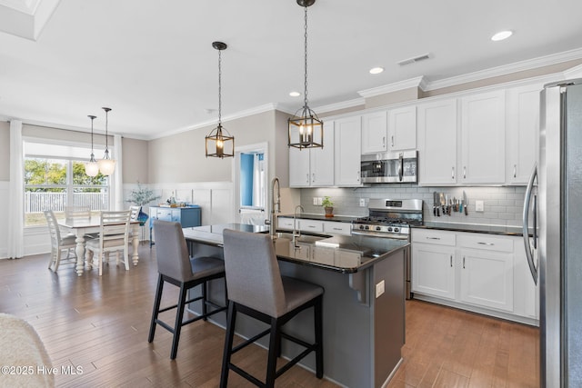 kitchen with decorative light fixtures, a center island with sink, appliances with stainless steel finishes, white cabinetry, and a kitchen breakfast bar