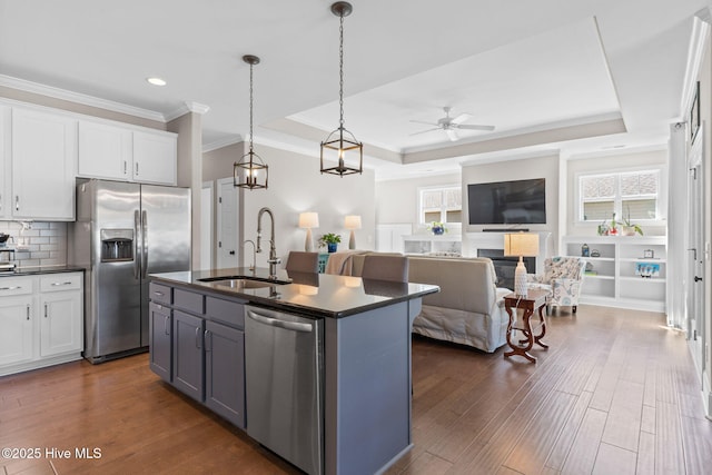 kitchen with white cabinets, a raised ceiling, dark countertops, appliances with stainless steel finishes, and a sink