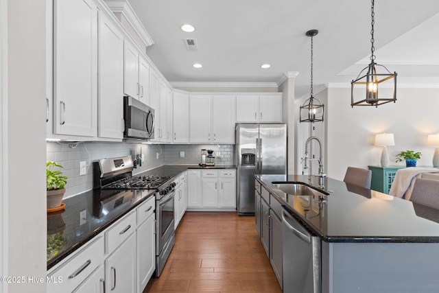 kitchen with stainless steel appliances, dark countertops, white cabinetry, and a kitchen island with sink