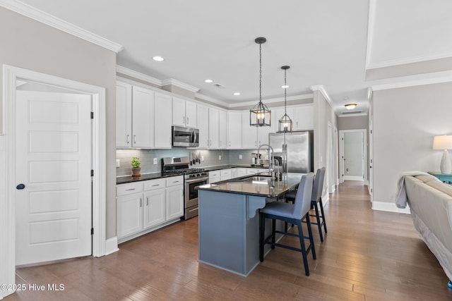 kitchen with stainless steel appliances, dark countertops, a kitchen island with sink, and white cabinets