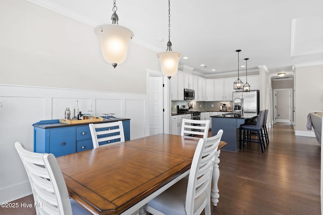 dining room with a wainscoted wall, a decorative wall, dark wood finished floors, and crown molding