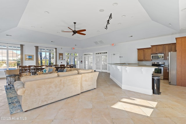 living room featuring a raised ceiling, visible vents, ornamental molding, a ceiling fan, and baseboards